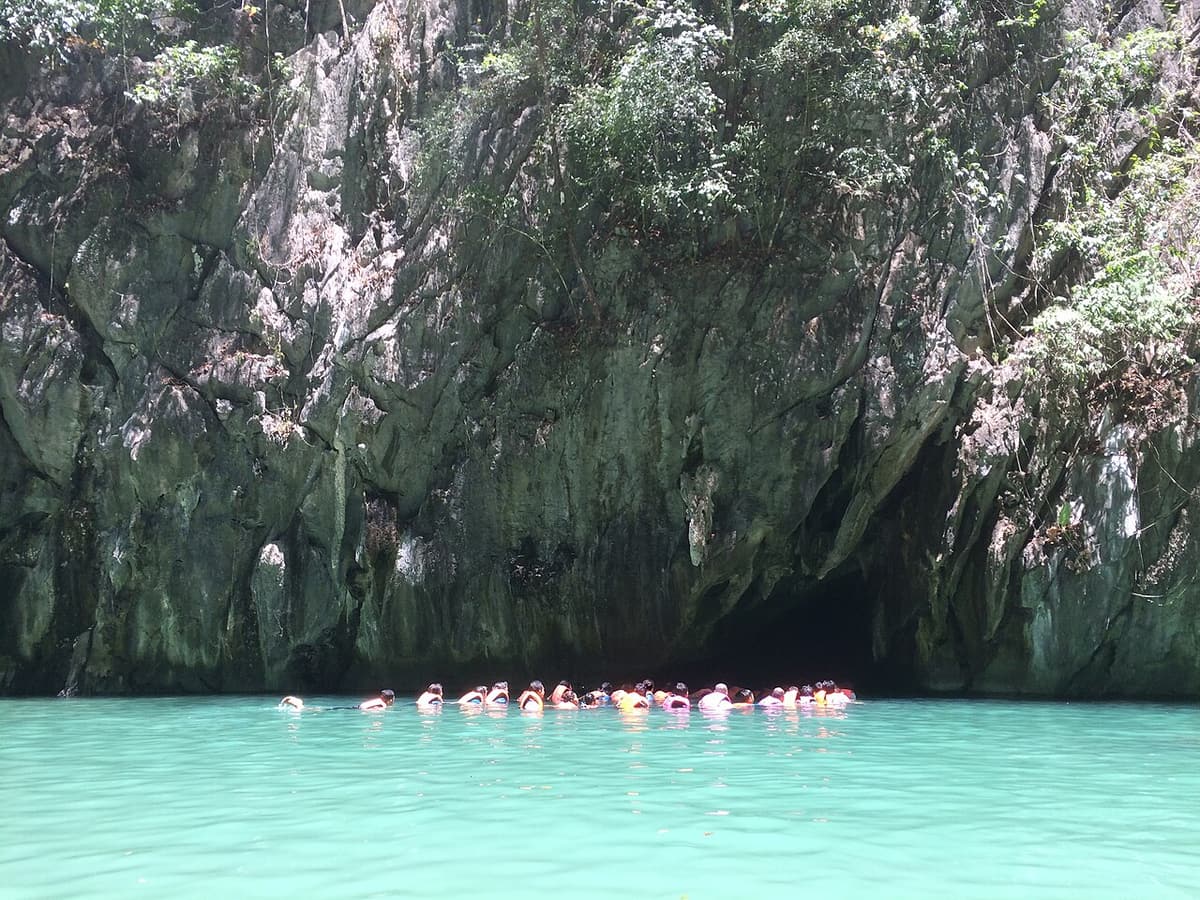 Swimmers in life jackets at the entrance of a sea cave in the limestone cliffs of Koh Muk