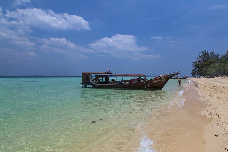 A wooden longtail boat pulled up on the white sand of Koh Kradan