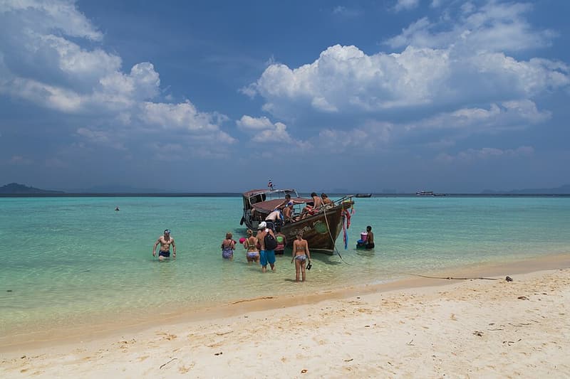 Snorkellers wading out to a longtail boat in the shallows off Koh Kradan